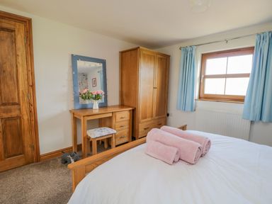 A bedroom with wooden furniture a bed with pink towels and a window with blue curtains at Bramblewood Cottage in Crookdake near Bassenthwaite