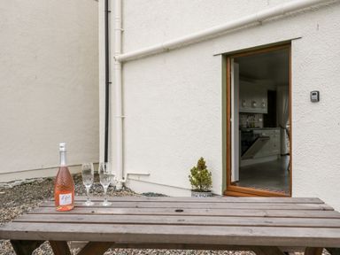 A wooden picnic table with a bottle of rose and two glasses outside a cottage with an open door showing a kitchen at Bramblewood Cottage in Crookdake near Bassenthwaite