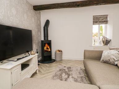 A living room with a sofa a wood burning stove and a television at Bella Cottage Bolton near Appleby-in-Westmorland