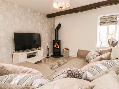A living room with a television on a white stand and a wood-burning stove at Bella Cottage Bolton near Appleby-in-Westmorland