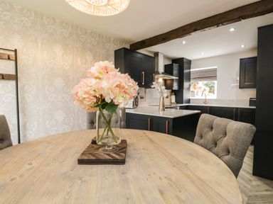 A kitchen with black cabinets a wooden round table with flowers in a glass vase and upholstered chairs at Bella Cottage in Bolton near Appleby-in-Westmorland