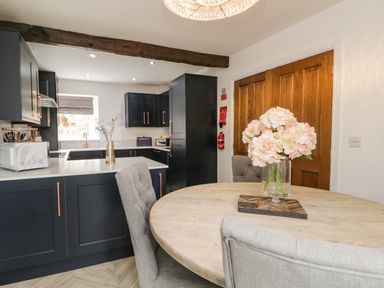 A kitchen and dining area with black cabinets and a round wooden table with flowers in a vase at Bella Cottage Bolton near Appleby-in-Westmorland
