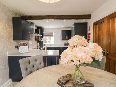 A kitchen with black cabinets and a wooden dining table with flowers in a vase at Bella Cottage Bolton near Appleby-in-Westmorland