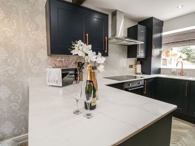 A kitchen with black cabinets white marble countertops a bottle of champagne two glasses a toaster and a window at Bella Cottage Bolton near Appleby-in-Westmorland