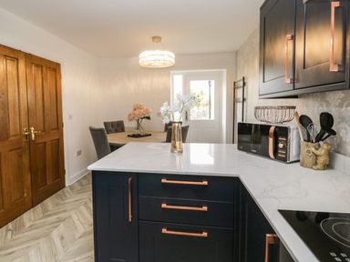 A kitchen area with dark cabinets and copper handles and a dining table with chairs and flowers at Bella Cottage in Bolton near Appleby-in-Westmorland