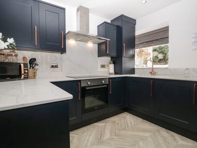 A kitchen with dark cabinets white countertops oven and a window with a flower vase at Bella Cottage Bolton near Appleby-in-Westmorland