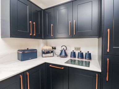 A kitchen corner with dark cabinets copper handles white marble countertop a toaster kettle canisters and a bread box at Bella Cottage Bolton near Appleby-in-Westmorland