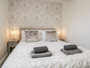 A bedroom with a bed white bedding two grey towels on the bed two bedside tables with lamps and patterned wallpaper at Bella Cottage Bolton near Appleby in Westmorland