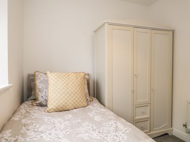 A bedroom with a single bed with patterned bedding and cushions next to a cream wardrobe at Bella Cottage Bolton near Appleby-in-Westmorland