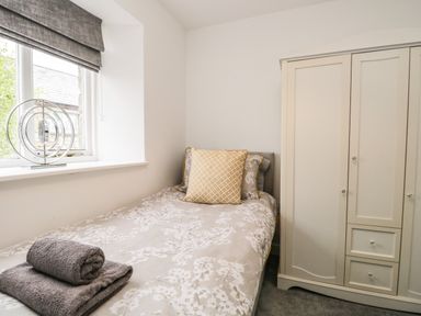 A bedroom with a single bed with patterned bedding and a pillow next to a window and a wardrobe at Bella Cottage Bolton near Appleby-in-Westmorland