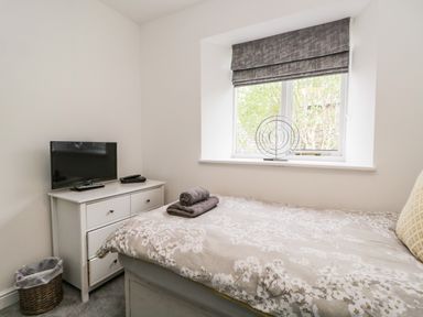 A small bedroom with a bed a window with blinds a chest of drawers with a television and a waste basket at Bella Cottage in Bolton near Appleby-in-Westmorland