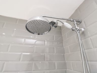 A shower area with a large round shower head and a smaller handheld shower head on tiled gray walls at Bella Cottage in Bolton near Appleby-in-Westmorland