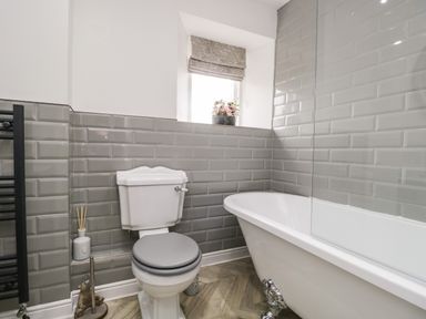 A bathroom with a toilet and a clawfoot bathtub with grey tiled walls at Bella Cottage Bolton near Appleby-in-Westmorland