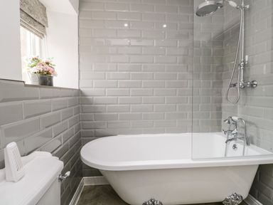 A bathroom with a freestanding bathtub shower and a window with flowers at Bella Cottage Bolton near Appleby-in-Westmorland