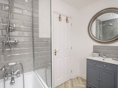 A bathroom with a bathtub shower combo a gray vanity with a round mirror and a white door at Bella Cottage Bolton near Appleby-in-Westmorland