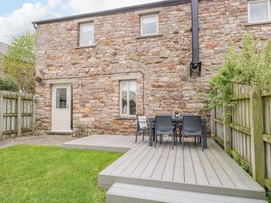 A stone house with a wooden deck patio with table and chairs in a fenced garden at Bella Cottage Bolton near Appleby-in-Westmorland