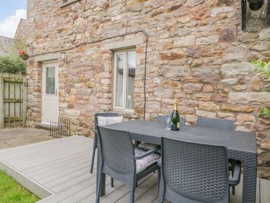 An outdoor patio area with a black table and six chairs next to a stone wall at Bella Cottage Bolton near Appleby-in-Westmorland