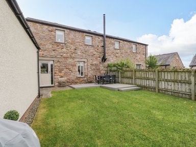 A backyard with grass lawn wooden deck with table and chairs stone house and wooden fence at Bella Cottage Bolton near Appleby-in-Westmorland
