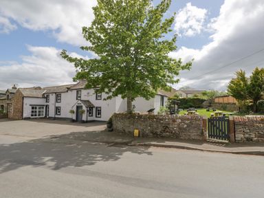 A white building with multiple windows and an entrance beside a large tree and a stone wall with a gated garden area at Bella Cottage Bolton near Appleby-in-Westmorland