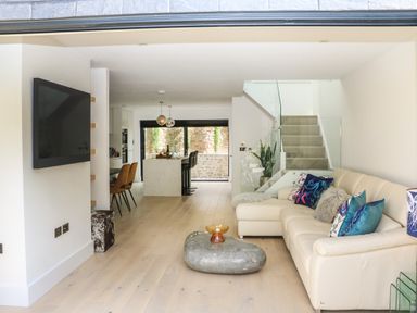 A living area with a beige sofa and colorful cushions a stone coffee table and stairs leading up at Sail Loft in Dawlish
