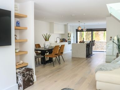 An open plan kitchen and dining area with a dining table and chairs kitchen island with bar stools and large windows at Sail Loft in Dawlish