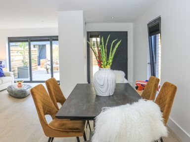 A dining table with chairs and a vase with flowers in a room with glass doors and wooden floor at Sail Loft in Dawlish