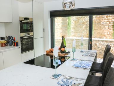 A kitchen with white countertop and black chairs set with placemats glasses and cutlery at Sail Loft in Dawlish