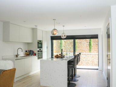 A modern kitchen with a marble island and bar stools next to a large window at Sail Loft in Dawlish