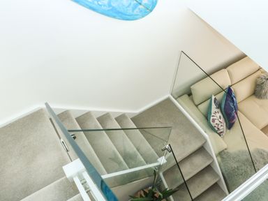 A carpeted staircase with glass railing next to a beige sofa with pillows at Sail Loft Dawlish
