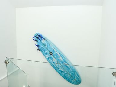 A blue surfboard leaning against a white wall behind a glass railing at Sail Loft in Dawlish