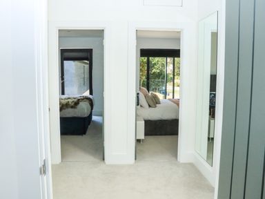 A hallway with two open doors leading to bedrooms and a wall mirror at Sail Loft in Dawlish
