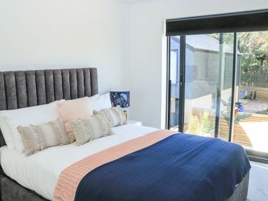 A bedroom with a grey upholstered bed with pillows and a blanket by a sliding glass door at Sail Loft in Dawlish