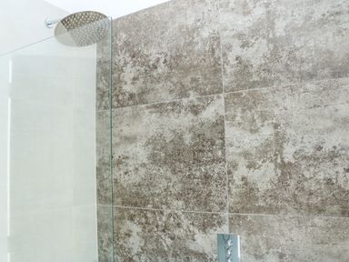 A shower area with large textured wall tiles a glass shower screen and a round rain shower head at Sail Loft in Dawlish