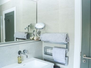 A bathroom sink area with towels on a wall-mounted rack and a round adjustable mirror at Sail Loft in Dawlish