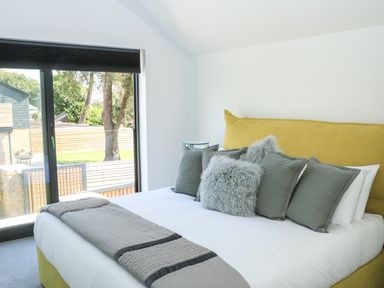 A bedroom with a yellow bed frame grey pillows and a window showing a garden at Sail Loft in Dawlish