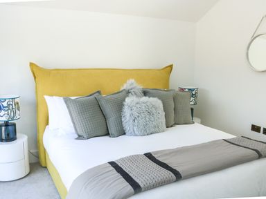 A bedroom with a mustard yellow bed frame grey pillows and bedside tables with lamps at Sail Loft in Dawlish