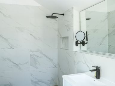 A bathroom with marble tiled walls a black showerhead a round mirror and a white sink at Sail Loft in Dawlish