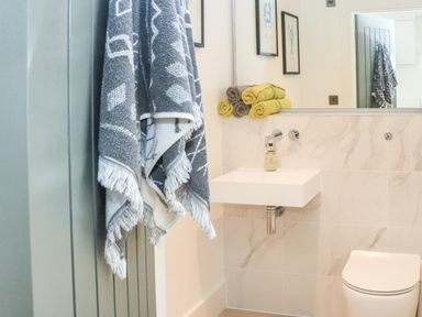 A bathroom with a wall-mounted sink, stacked towels, a hanging towel, and a toilet at Sail Loft in Dawlish