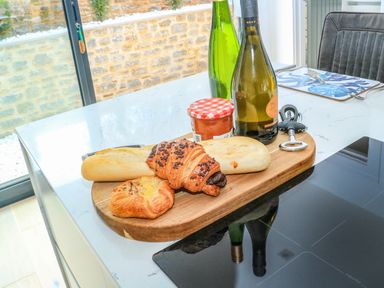 A kitchen countertop with a wooden board holding bread, pastries, a jar of jam, two bottles, and a corkscrew at Sail Loft in Dawlish