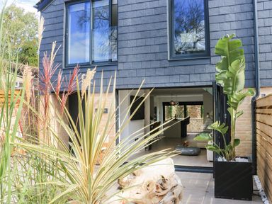 Plant pots outside a modern house with large windows and an open sliding door showing the interior at Sail Loft in Dawlish
