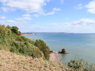 A coastal cliff with green vegetation overlooking a beach and sea with distant hills at Sail Loft in Dawlish