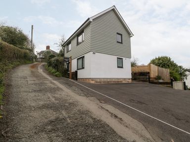 A house with grey siding and white lower walls next to a steep gravel road at Sevenwoods View in Longhope