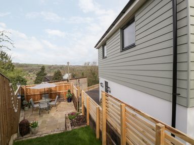 An outdoor patio with table chairs and umbrella next to a house with hill views at Sevenwoods View in Longhope