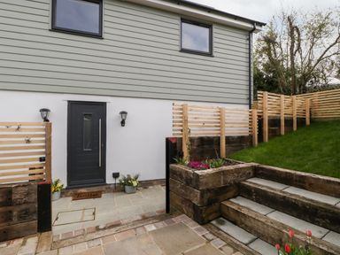 An exterior view of a house with a black door two wall lights a doormat and wooden steps leading to a grassy area at Sevenwoods View in Longhope
