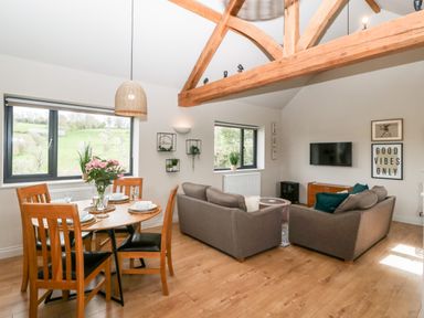 A living and dining area with wooden dining table and chairs a gray sofa set a wall mounted tv and visible wooden ceiling beams at Sevenwoods View in Longhope