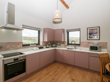 A kitchen with mauve cabinets wooden floor two windows stove oven and microwave at Sevenwoods View in Longhope