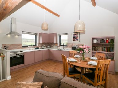 A kitchen and dining area with pink cabinets wooden dining table and chairs and a bookshelf at Sevenwoods View in Longhope