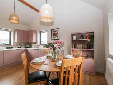 A kitchen dining area with a round wooden table set for four and pink cabinets at Sevenwoods View in Longhope