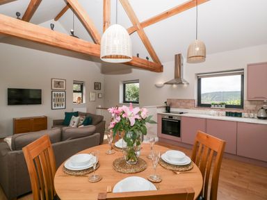 A dining table with plates and flowers in an open plan kitchen and living area with wooden beams at Sevenwoods View in Longhope