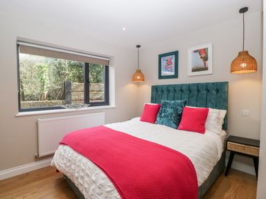 A bedroom with a bed featuring teal and pink cushions and a pink throw at Sevenwoods View in Longhope